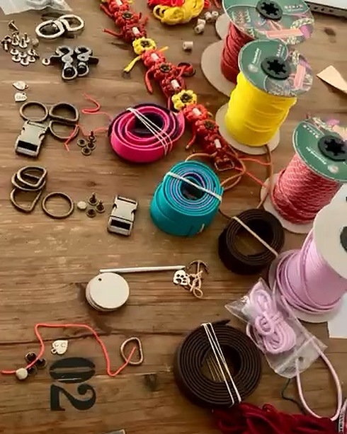 L'établi vu de dessus&nbsp;: bobines de paracorde, rouleaux de cuir vegan, boucles, anneaux, rivets, médaillons Roxika et une pièce fleurs en cours