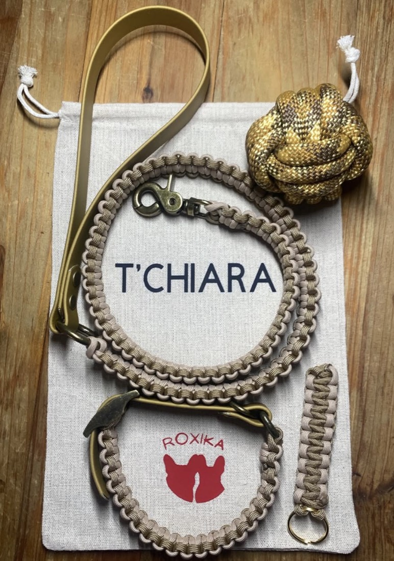 Un pack posé à plat sur son pochon en coton au prénom T'Chiara : collier et harnais tressés beige et sable, laisse en cuir vegan doré, Crazy Ball assortie et porte-clés tressé
