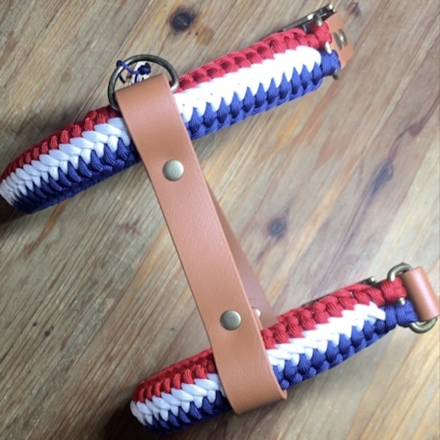 Harnais H à plat, replié&nbsp;: deux sangles en cuir vegan marron clair rivetées sur un tressage bleu blanc rouge, avec l'anneau pour la laisse et la boucle ajustable en finition antique