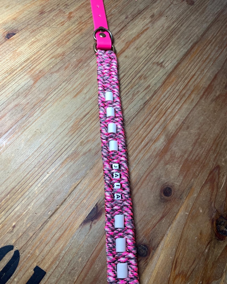 Collier trilo rose à plat&nbsp;: perles-lettres blanches formant un prénom, glissées entre les perles de céramique EM